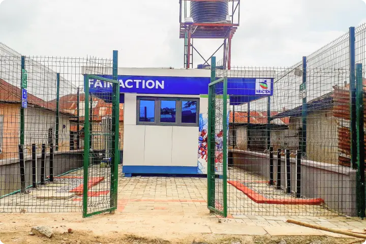 A fenced water station with a blue and white sign, surrounded by buildings, featuring a large water tank on top.