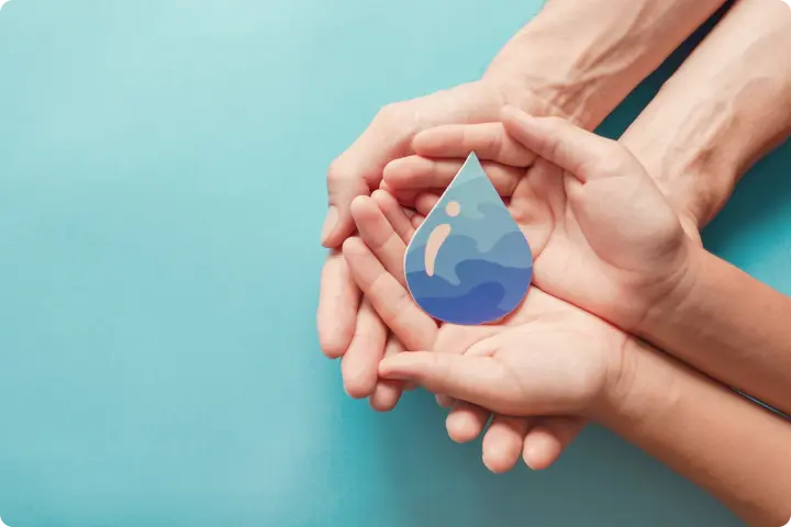 Hands holding a blue water droplet cutout against a light blue background, symbolizing water conservation and protection.