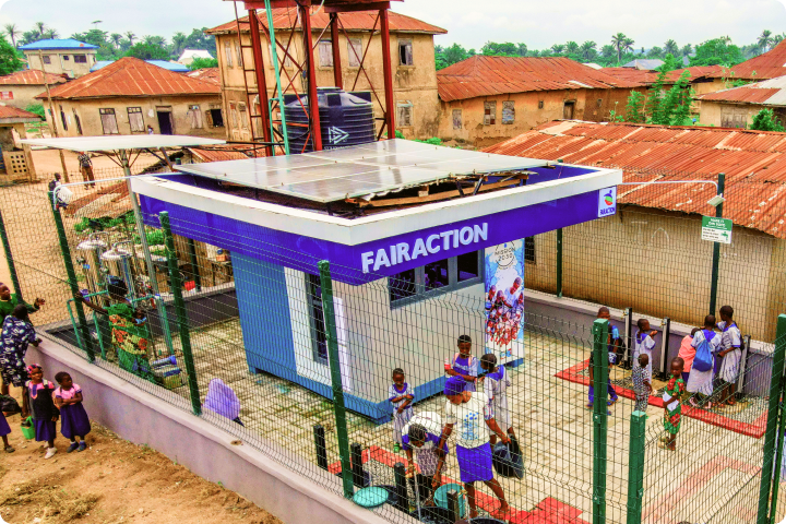 A fenced, solar-powered water kiosk labeled "FAIRACTION," with children and adults gathering around in a rural setting.