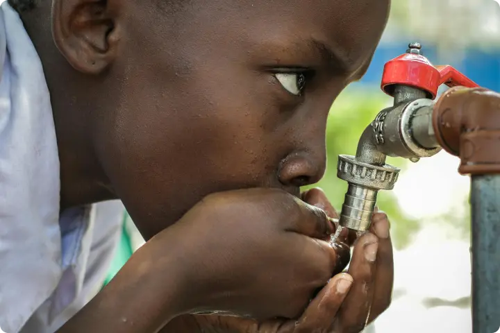 Child drinking water from a faucet, cupping hands to catch the flow, with a focused expression.