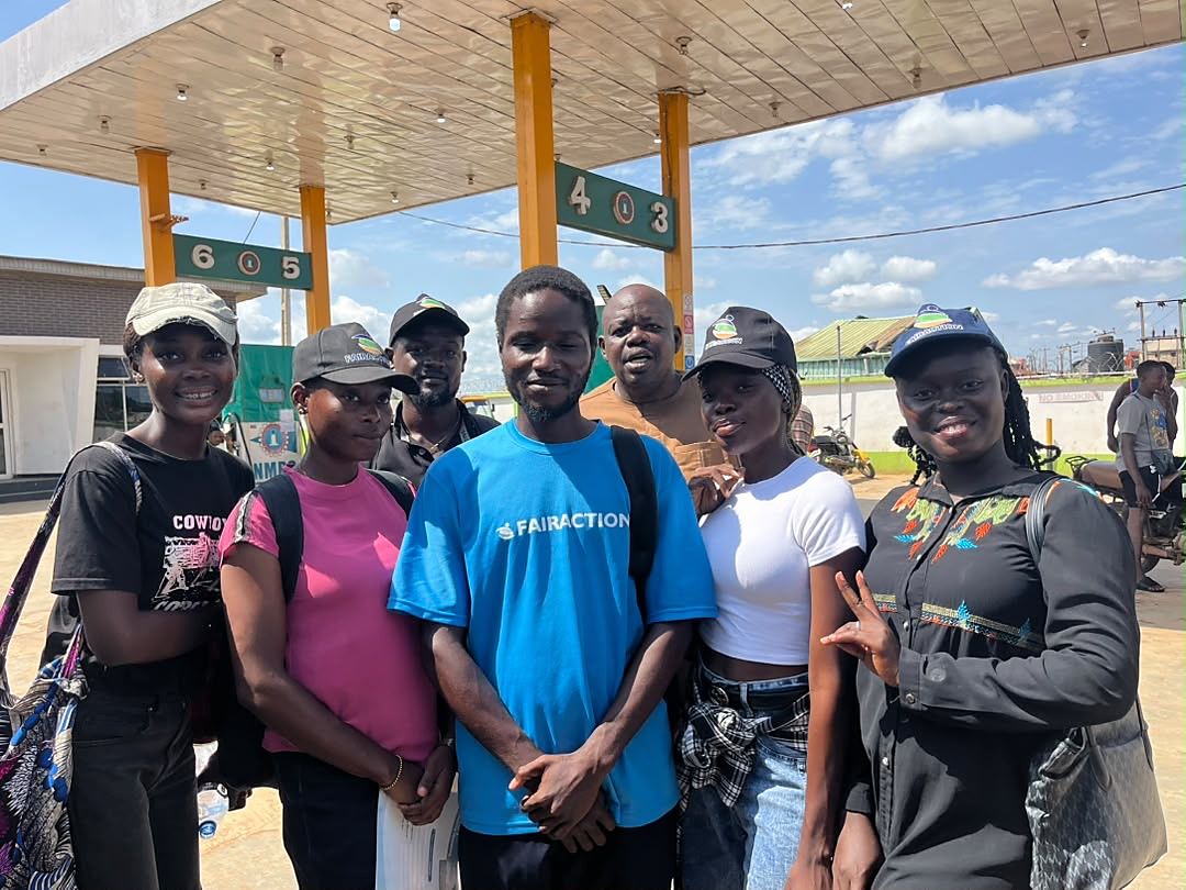 Seven Fairaction field researchers in caps and Fairaction shirts, standing together under a canopy at the end of a day of field work during the Oyo State mapping.